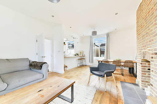 Bright living space with white walls, a grey sofa, timber flooring and an exposed brick wall, shown in David Jenkins's interior-painting Google review.