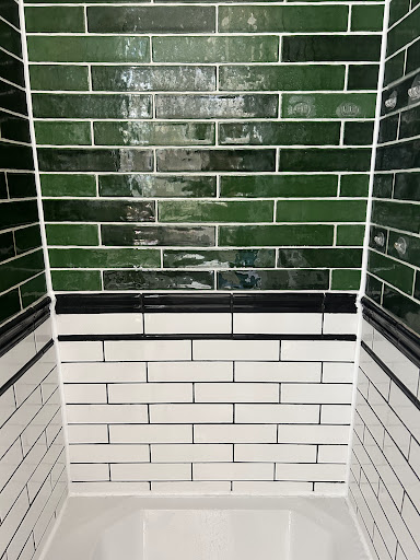 Shower alcove with green upper tiles, white lower tiles and dark trim, shown in Justin Hervel's Google review.